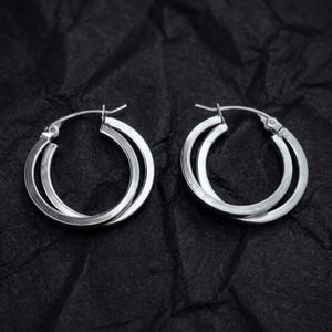 May include: A pair of silver-toned hoop earrings featuring a double-layered design. Each earring consists of two interlocking circular bands with a polished metallic finish and a hinged post closure mechanism at the top of the hoop structure.
