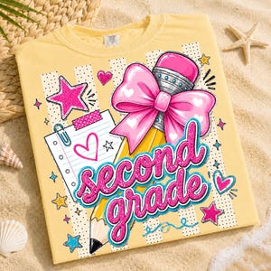 May include: A pale yellow t-shirt featuring a graphic print of a yellow pencil with a large pink bow, a piece of lined notebook paper with a heart, and the text second grade in glittery pink letters, surrounded by stars and small hearts.