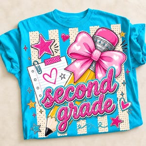 May include: A bright turquoise t-shirt featuring a graphic print of a yellow pencil with a large pink bow, a lined notepad with a paperclip, and the text "second grade" in glittery pink script, surrounded by pink and yellow stars and hearts.