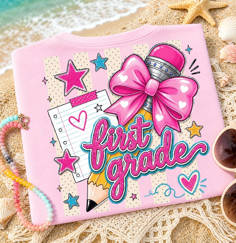 May include: A light pink t-shirt featuring a graphic print of a yellow pencil with a large pink bow, a piece of lined notebook paper with a heart, and the text "first grade" in bright pink glittery script, surrounded by small stars and hearts.