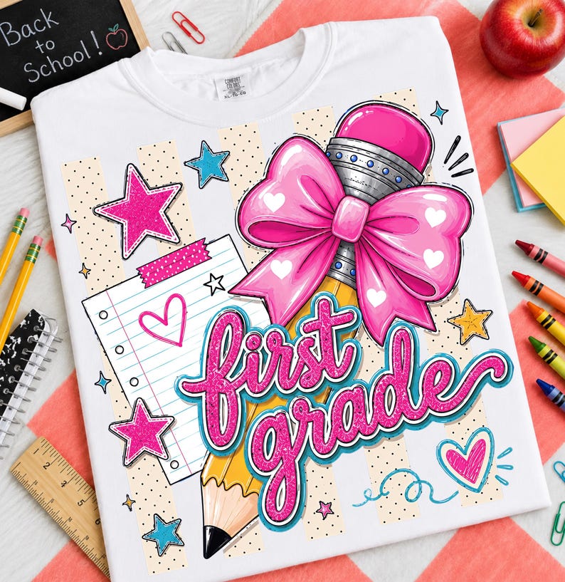 May include: A white t-shirt featuring a graphic print with the text first grade in pink glittery script. The design includes a large pink bow, a yellow pencil, a lined notebook page, pink and blue stars, and hearts on a beige striped background.