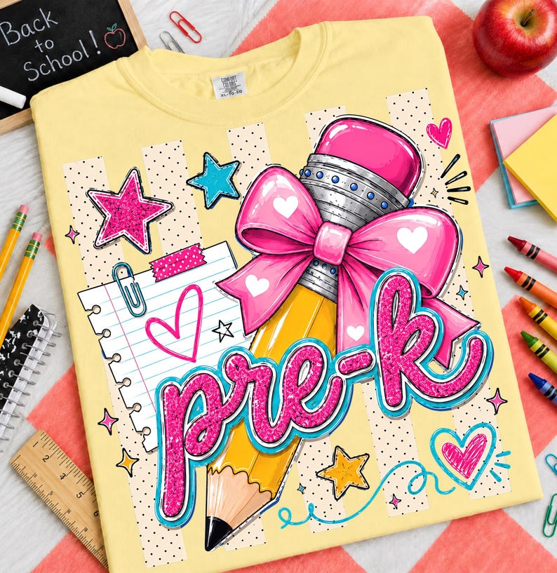 May include: A pale yellow t-shirt featuring a graphic print of a yellow pencil with a large pink bow, a piece of lined notebook paper, and the text "pre-k" in glittery pink script. The design includes pink and blue stars and hearts.