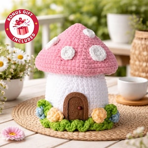 May include: A handmade crochet mushroom house with a pink cap and white spots. The house has a white base, a brown door, and is surrounded by green, blue, and yellow crochet flowers. The image includes a "BONUS GIFT INCLUDED" sticker.