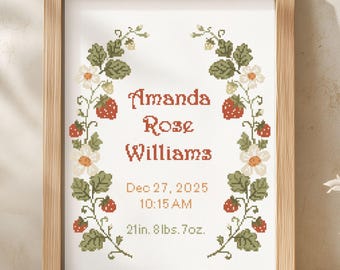 May include: A framed cross-stitch birth announcement featuring a strawberry vine border with red berries and white flowers. The text reads Amanda Rose Williams, Dec 27, 2025, 10:15 AM, 21in. 8lbs. 7oz. in a light wood frame with a clean white background.