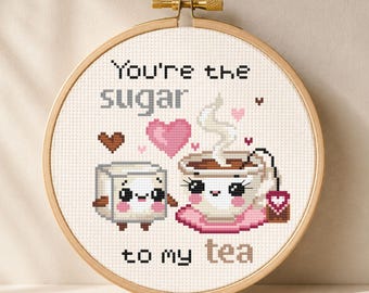 May include: Cross-stitch embroidery in a wooden hoop. The design features a smiling sugar cube and a teacup with the text "You're the sugar to my tea". The color palette includes pink, brown, and white.