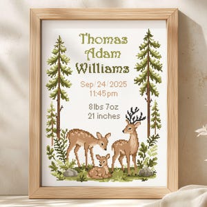 May include: A framed cross-stitch birth announcement featuring a forest scene with three deer, pine trees, and ferns. The text reads Thomas Adam Williams, Sep/24/2025, 11:45pm, 8lbs 7oz, and 21 inches. The design uses shades of green, brown, and tan.