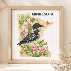 May include: A square framed cross-stitch embroidery featuring the state of Minnesota in a pale yellow hue. The design includes a black and white loon, pink lady slipper flowers, green foliage, and small orange stars with the text MINNESOTA.
