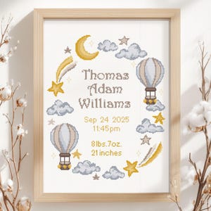 May include: A framed cross-stitch birth announcement featuring the name Thomas Adam Williams, date 24 Sep 2025, time 11:45 pm, weight 8lbs 7oz, and length 21 inches. The design includes yellow stars, a crescent moon, and two hot air balloons.