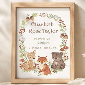 May include: A framed cross-stitch artwork featuring woodland animals and the name "Elizabeth Rose Taylor" with birth details. The design includes a deer, fox, and bear, surrounded by a floral wreath. The frame is light wood.