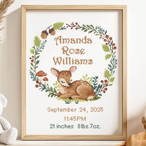 May include: A framed cross-stitch artwork featuring a sleeping fawn surrounded by a floral wreath. The artwork includes the name "Amanda Rose Williams" and birth details: September 24, 2025, 11:45 PM, 53.3 cm, 3.8 kg. The frame is made of light wood.