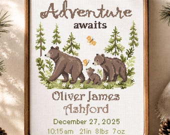 May include: A framed cross-stitch sampler featuring the text Adventure awaits, the name Oliver James Ashford, and the birth details December 27, 2025, 10:15am, 21in, 8lbs 7oz. The design includes two brown bears, a cub, pine trees, and butterflies.