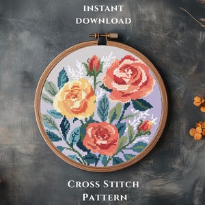 Op de afbeelding: Een kruissteekpatroon met een bloemmotief, met oranje en gele rozen, groene bladeren en witte accenten, geplaatst in een houten borduurring. De tekst "INSTANT DOWNLOAD" en "CROSS STITCH PATTERN" zijn zichtbaar.
