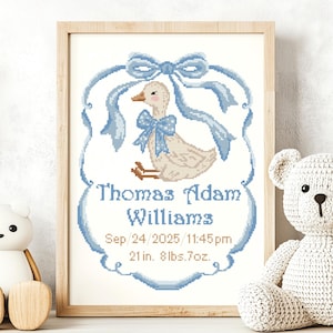May include: A framed cross-stitch birth announcement featuring a light brown duck with a blue polka-dot bow, framed by a blue ribbon border. The text reads Thomas Adam Williams, Sep 24 2025 11:45pm, 21 in. 8lbs.7oz. in blue and brown lettering.