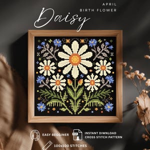 May include: A framed cross-stitch pattern featuring a daisy design. The artwork includes white daisies with orange centers, blue flowers, and green foliage on a black background. The text reads "Daisy" and "April Birth Flower".