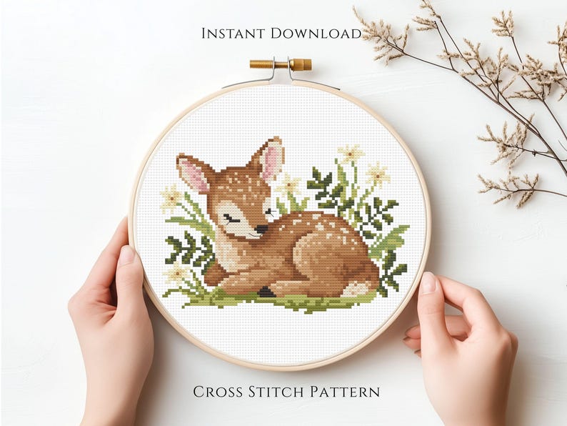 May include: A cross stitch pattern of a sleeping fawn surrounded by flowers and greenery, set within a wooden embroidery hoop. The text "INSTANT DOWNLOAD" and "CROSS STITCH PATTERN" are visible.
