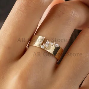 Puede incluir: Un anillo dorado con una banda plana y un diseño floral. El anillo presenta pequeñas piedras preciosas transparentes. El texto "AR Gold Store" es visible en el anillo.