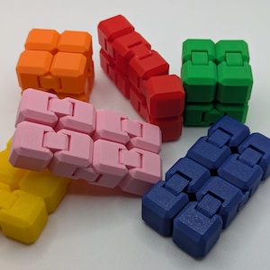 May include: A selection of colourful fidget toys in orange, red, green, pink, yellow, and blue. Each toy is made of connected, articulated cubes. The toys are arranged on a white surface.