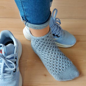 Puede incluir: Un calcetín de punto azul claro con un patrón de diamantes se usa con zapatillas azules. Las zapatillas tienen suelas y cordones blancos. La persona lleva vaqueros azules.