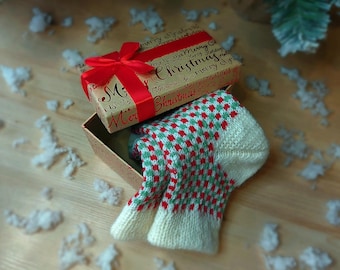 以下が含まれることがあります： 赤いリボンが付いたクリスマスギフトボックス。中には、赤と緑のひし形模様のクリーム色の靴下が入っています。ギフトボックスは「Merry Christmas」の文字が入ったお祝いの紙で包まれています。