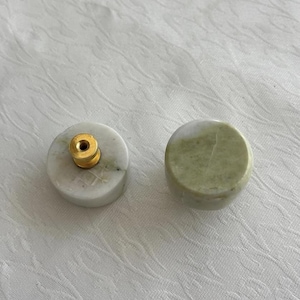 Könnte beinhalten: Zwei dekorative Stein-Knöpfe. Einer ist weiß mit einer goldfarbenen Metallschraube, der andere ist ein massiver grüner Stein. Die Knöpfe sind rund und scheinen aus Marmor oder einem ähnlichen Stein zu bestehen. Sie sind wahrscheinlich für Möbel oder Schränke.