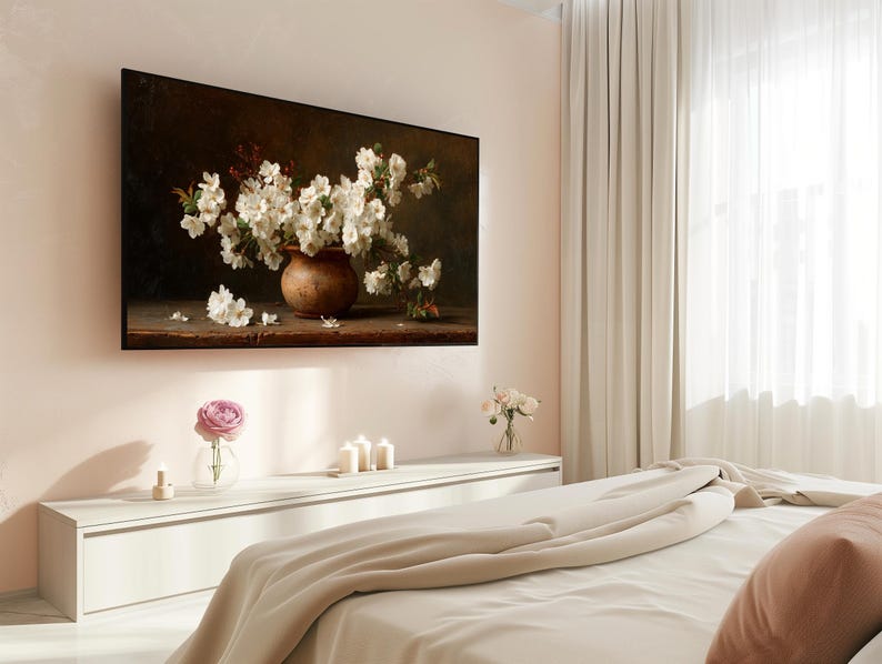 Puede incluir: Una pintura enmarcada representa una naturaleza muerta de flores blancas en un jarr&oacute;n marr&oacute;n. La obra de arte est&aacute; montada en una pared rosa claro sobre una c&oacute;moda blanca. Una sola rosa rosa en un jarr&oacute;n de cristal est&aacute; sobre la c&oacute;moda.