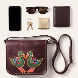 The Moruda Sling shown with a smartphone, folded sunglasses, a bifold wallet, keys and a compact mirror to show what it holds (AI-generated)