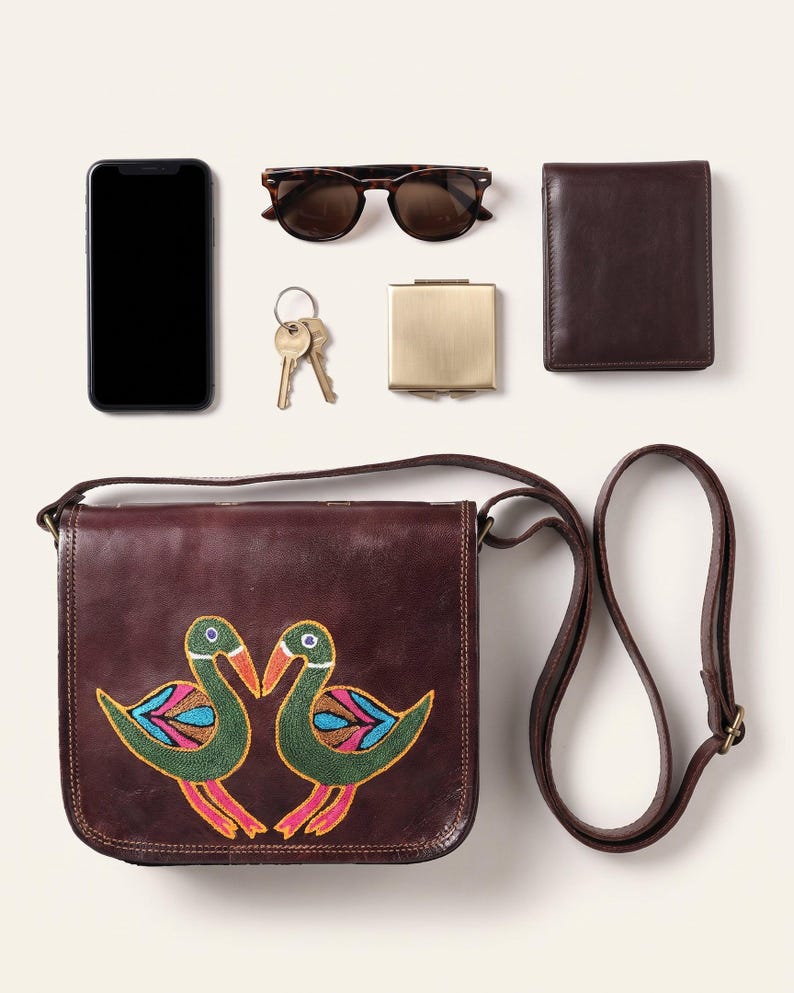 The Moruda Sling shown with a smartphone, folded sunglasses, a bifold wallet, keys and a compact mirror to show what it holds (AI-generated)