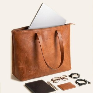 A 16-inch laptop sliding into The Abhaneri Tote, with a notebook, pen, glasses, cardholder and cables laid alongside