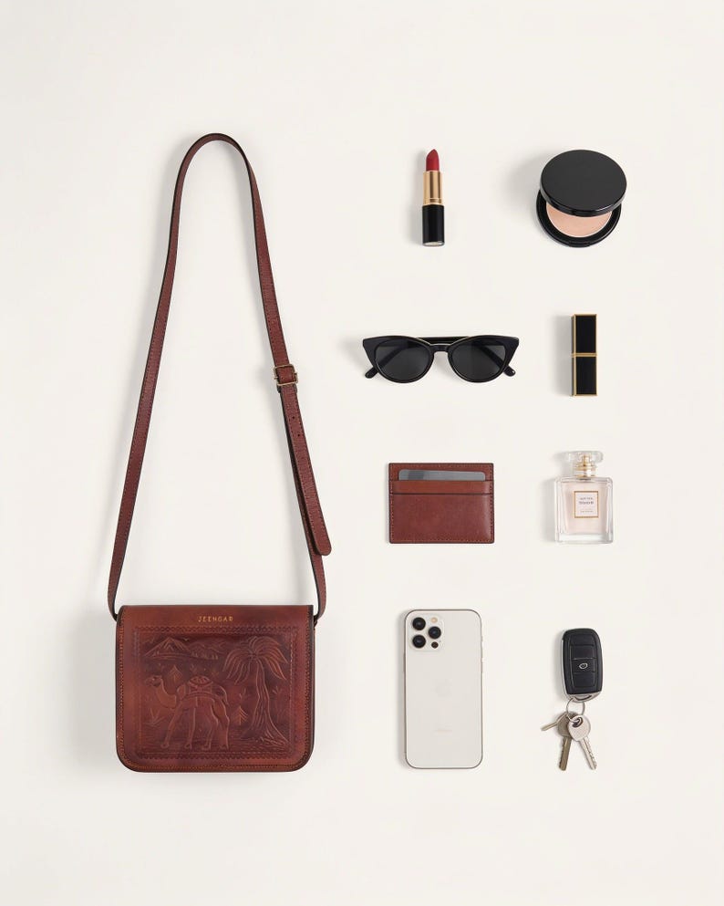 What The Jaisalmer Sling holds in Cherry: a lipstick, a powder compact, sunglasses, a cardholder, a perfume bottle, a phone and keys laid out beside the bag (AI-generated)