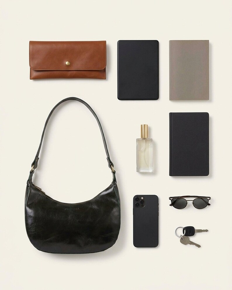 The Ranisar Shoulder Bag in dark olive, shown with a clutch, e-reader, paperback, perfume bottle, phone, sunglasses and keys to show what it holds (AI-generated)