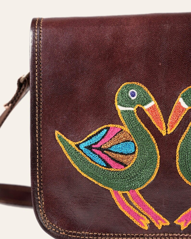 Close-up of the hand-embroidered birds on the Moruda Sling, green, turquoise and rose chain stitch