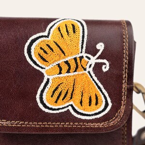 Close-up of the hand-embroidered golden butterfly on the cherry-brown leather flap