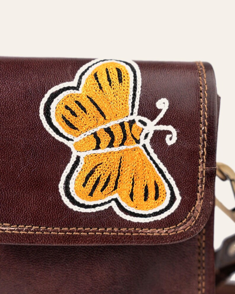 Close-up of the hand-embroidered golden butterfly on the cherry-brown leather flap