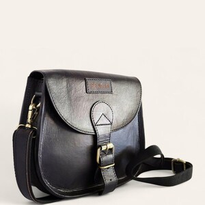 The Marwari Sling in Black, three-quarter view with the buckled flap and clip-on strap