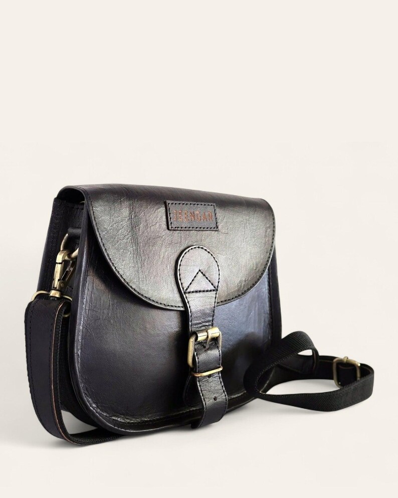 The Marwari Sling in Black, three-quarter view with the buckled flap and clip-on strap