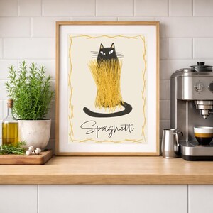 Puede incluir: Una impresi&oacute;n art&iacute;stica enmarcada que presenta un gato negro con espaguetis como pelaje. El gato est&aacute; sobre un fondo crema con un borde dorado. La palabra "Spaghetti" est&aacute; escrita debajo del gato en una fuente de escritura. La obra de arte se exhibe sobre una encimera de madera.