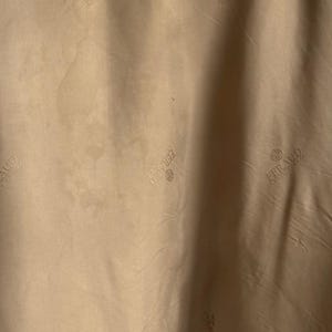 May include: A light tan fabric featuring a repeating pattern of the word FERAUD printed in a darker tan shade. The text is accompanied by a small circular logo above the brand name, creating a subtle, monochromatic design across the material.