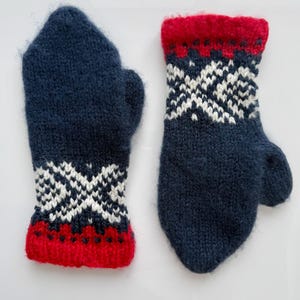 Peut inclure: Une paire de mitaines en tricot bleu marine avec un motif géométrique blanc et des poignets rouges. Les mitaines sont faites d'un fil doux et texturé, parfaites pour garder les mains au chaud.