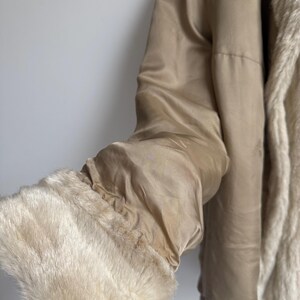 May include: A beige jacket featuring a smooth satin-like finish on the exterior and a plush, cream-colored faux fur lining. The sleeve ends in a wide, thick cuff made of the same soft, cream-colored faux fur material, providing a textured contrast.