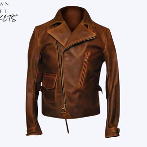 Pode incluir: Casaco de couro castanho com um design clássico de zíper assimétrico. Possui gola entalhada, um bolso pequeno e um bolso no peito com zíper. O texto "CROWN CRAFT JACKETS" é visível no canto superior esquerdo.
