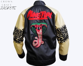 May include: Black satin jacket with cream-colored sleeves and black cuffs. The back features a large embroidered cobra design with the text "King Fury" in red. The sleeves have black embroidered patterns. The brand name "Crown Craft Jackets" is in the upper left corner.
