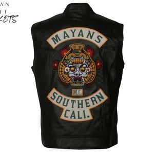 Op de afbeelding: Zwarte leren vest met een groot geborduurd embleem op de rug. Het embleem heeft de tekst "MAYANS" boven een gedetailleerde afbeelding van een schedel en de tekst "SOUTHERN CALI" eronder. Het vest heeft de tekst "CROWN CRAFT JACKETS" in de linkerbovenhoek.