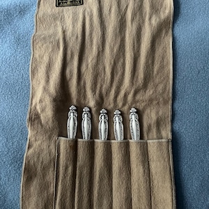 May include: A tan felt silverware roll with five silver utensils visible. The utensils have ornate handles. The roll has a label that reads "Daniel Low & Co. Jewelers & Silversmiths Salem, Mass. USA."