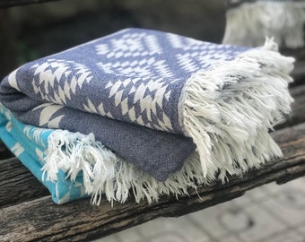 May include: Two folded patterned towels with white fringe. The top towel is blue with a white geometric design. The bottom towel is turquoise with a white geometric design.