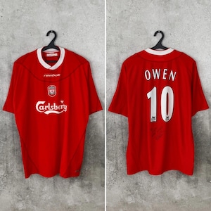 May include: A red Liverpool soccer jersey with white accents, featuring the Carlsberg logo and the Reebok brand. The back displays "OWEN" and the number "10". The jersey is hanging on a black hanger.