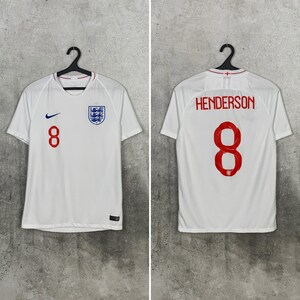 May include: A white England national soccer team jersey featuring the number 8 in red on the front and back. The front displays a blue Nike swoosh and the England crest. The back shows the name HENDERSON above the large red number 8.