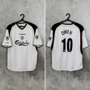 May include: White and black soccer jersey with the text "Carlsberg" and "Reebok". The jersey has black accents on the shoulders and sleeves. The back of the jersey has the name "Owen" and the number "10".