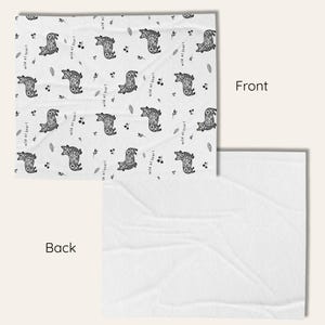 May include: A white blanket with a repeating pattern of stylized black bears and sprigs. The words "wild at heart" are printed in black. The back of the blanket is plain white.