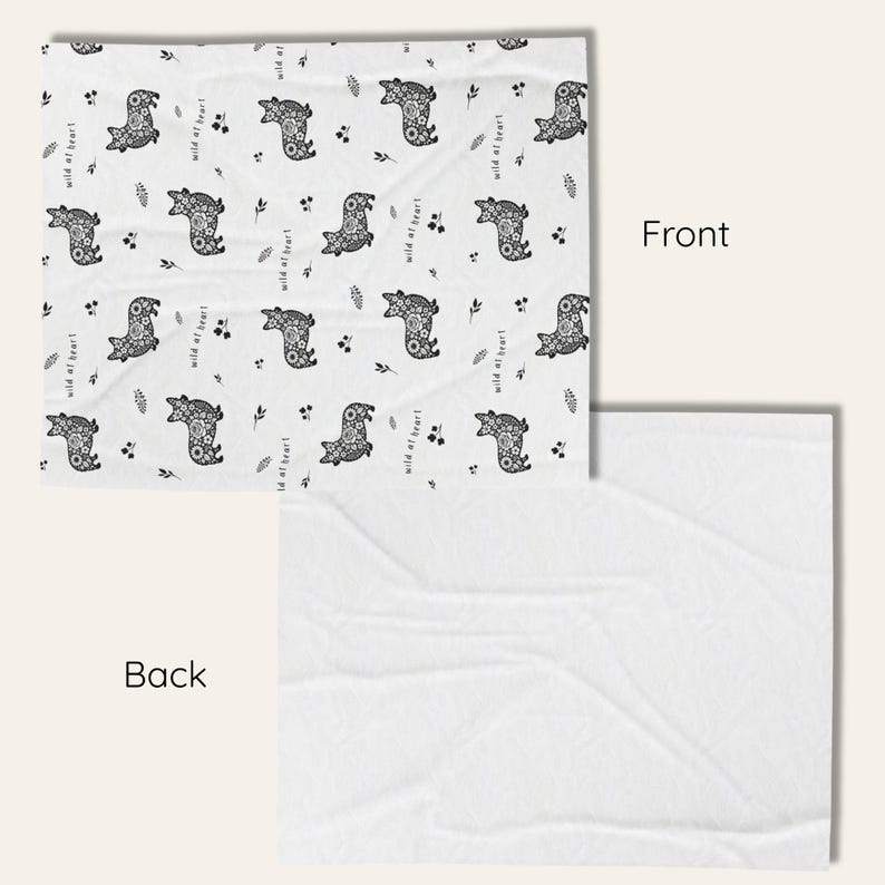 May include: A white blanket with a repeating pattern of stylized black bears and sprigs. The words "wild at heart" are printed in black. The back of the blanket is plain white.
