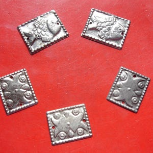 May include: Five rectangular silver-toned metal plates with embossed designs. Two plates feature a fish motif, while three plates display a symmetrical floral-like pattern. Each piece has a scalloped border and small holes for attachment.
